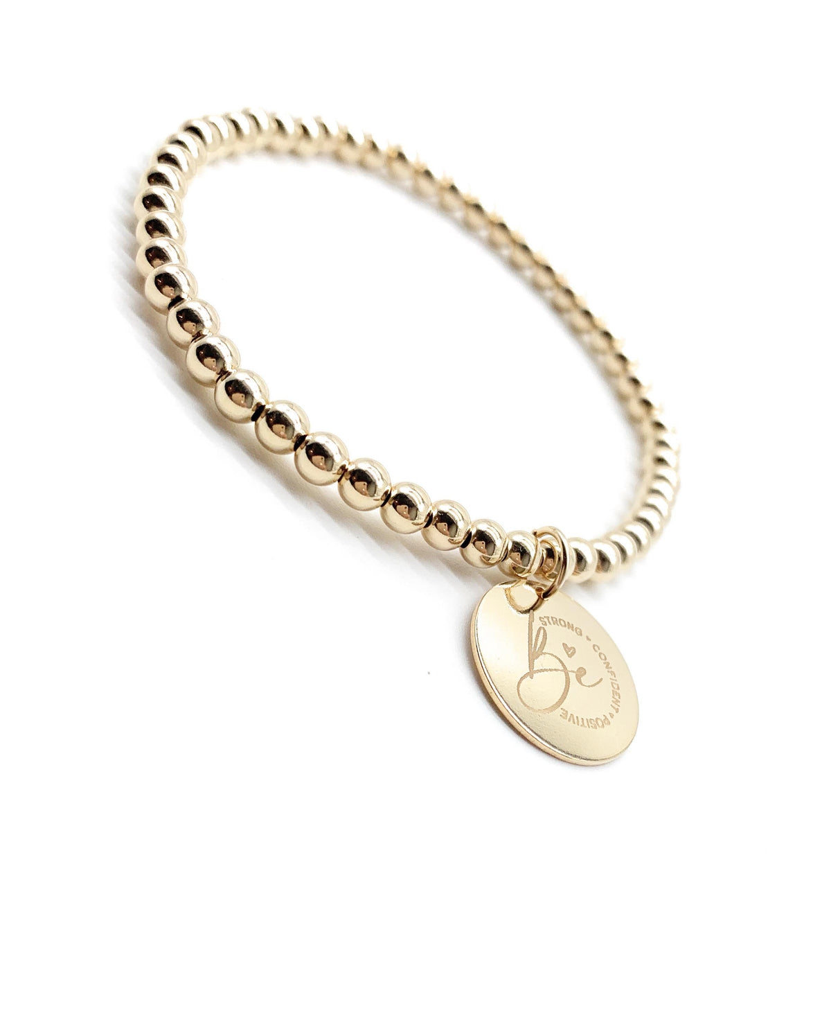 A gold beaded stretch bracelet with a round engraved initial charm displaying 'Be', set against a plain white background.