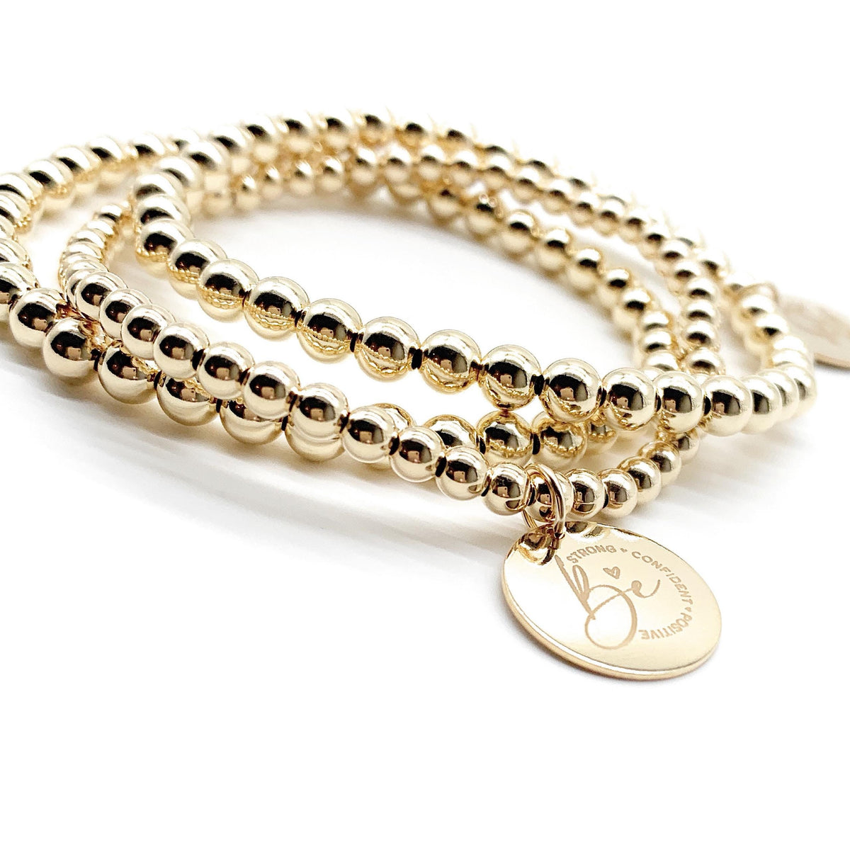 A gold beaded wrap bracelet with a round engraved disc charm, photographed on a clean white background.