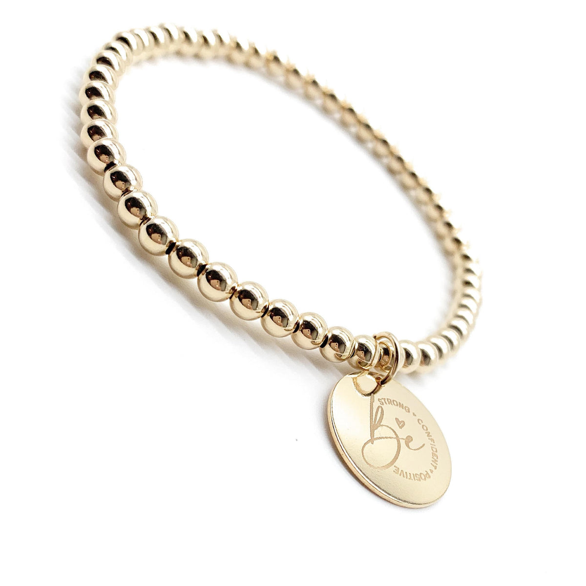 A gold beaded stretch bracelet with a round engraved disc charm, photographed on a clean white background.