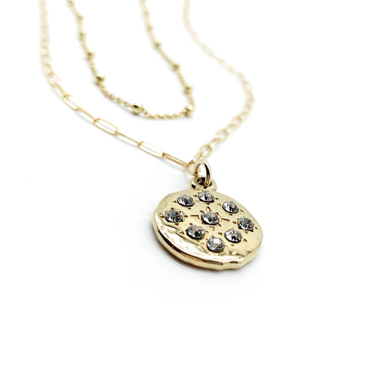 Gold necklace with a round pendant featuring small stones on a white background
