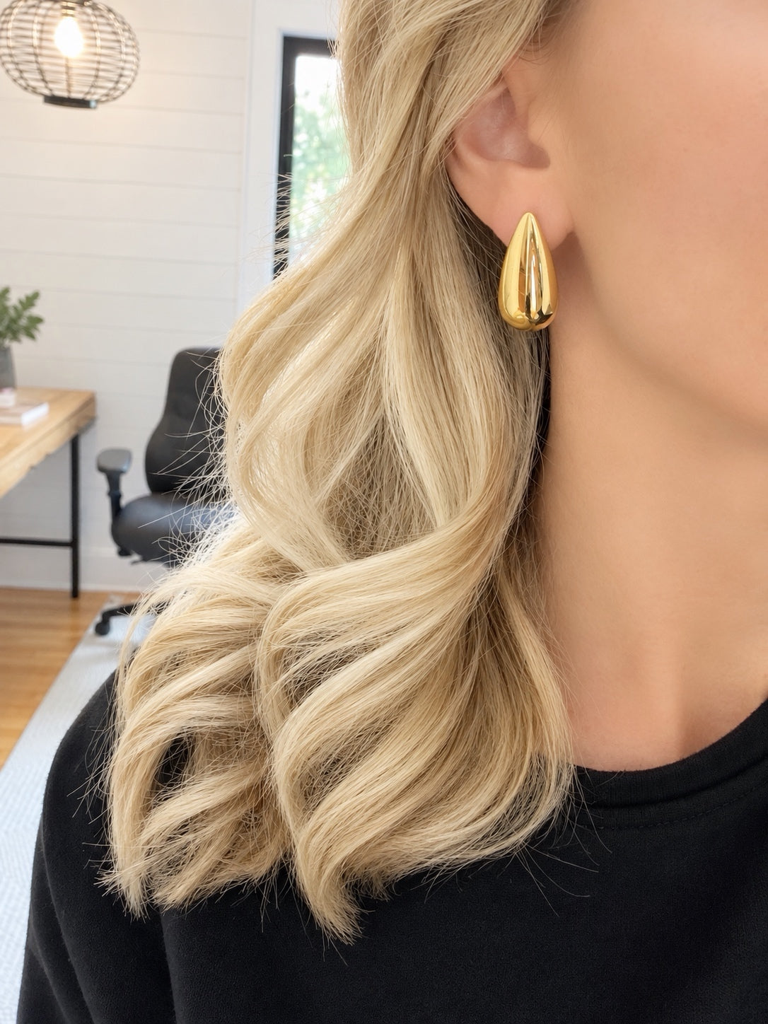 Polished gold-plated elongated teardrop earring worn on an ear