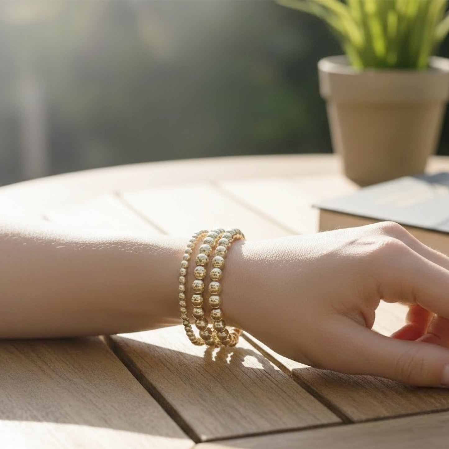 Hand wearing multiple 14 gold filled beaded bracelets on a wooden surface with a blurred background
