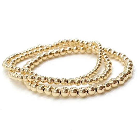 Three gold beaded stretch bracelets coiled together on a white background.
