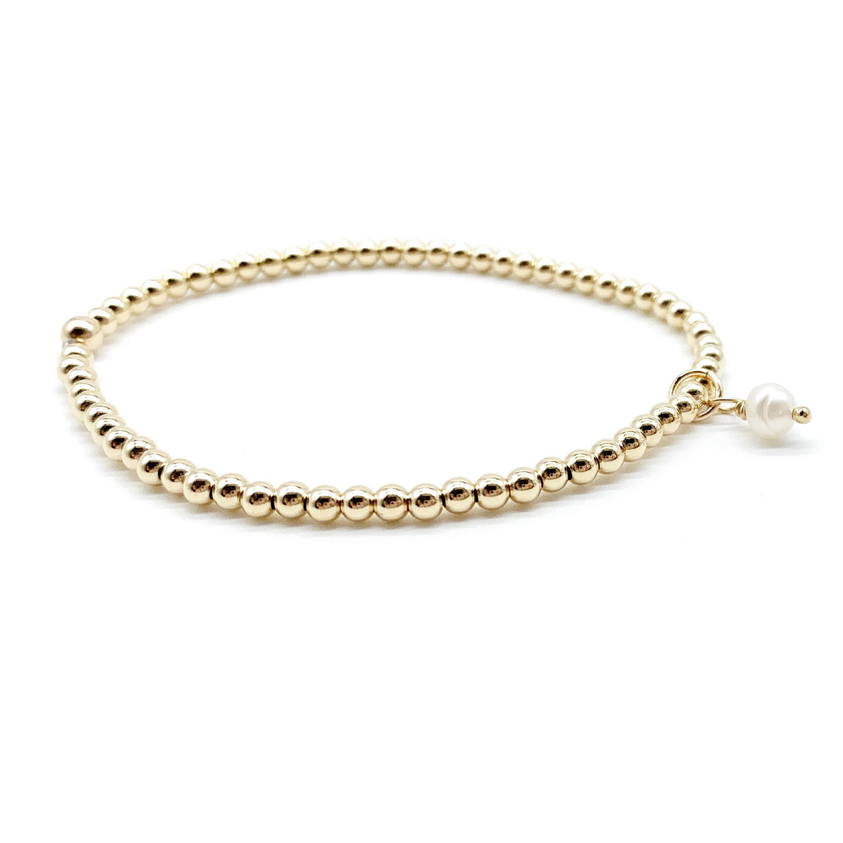 A gold beaded bracelet with a small white pearl drop charm, displayed on a clean white background.