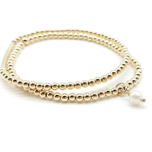 A gold beaded wrap bracelet with a small white pearl charm, displayed on a clean white background.